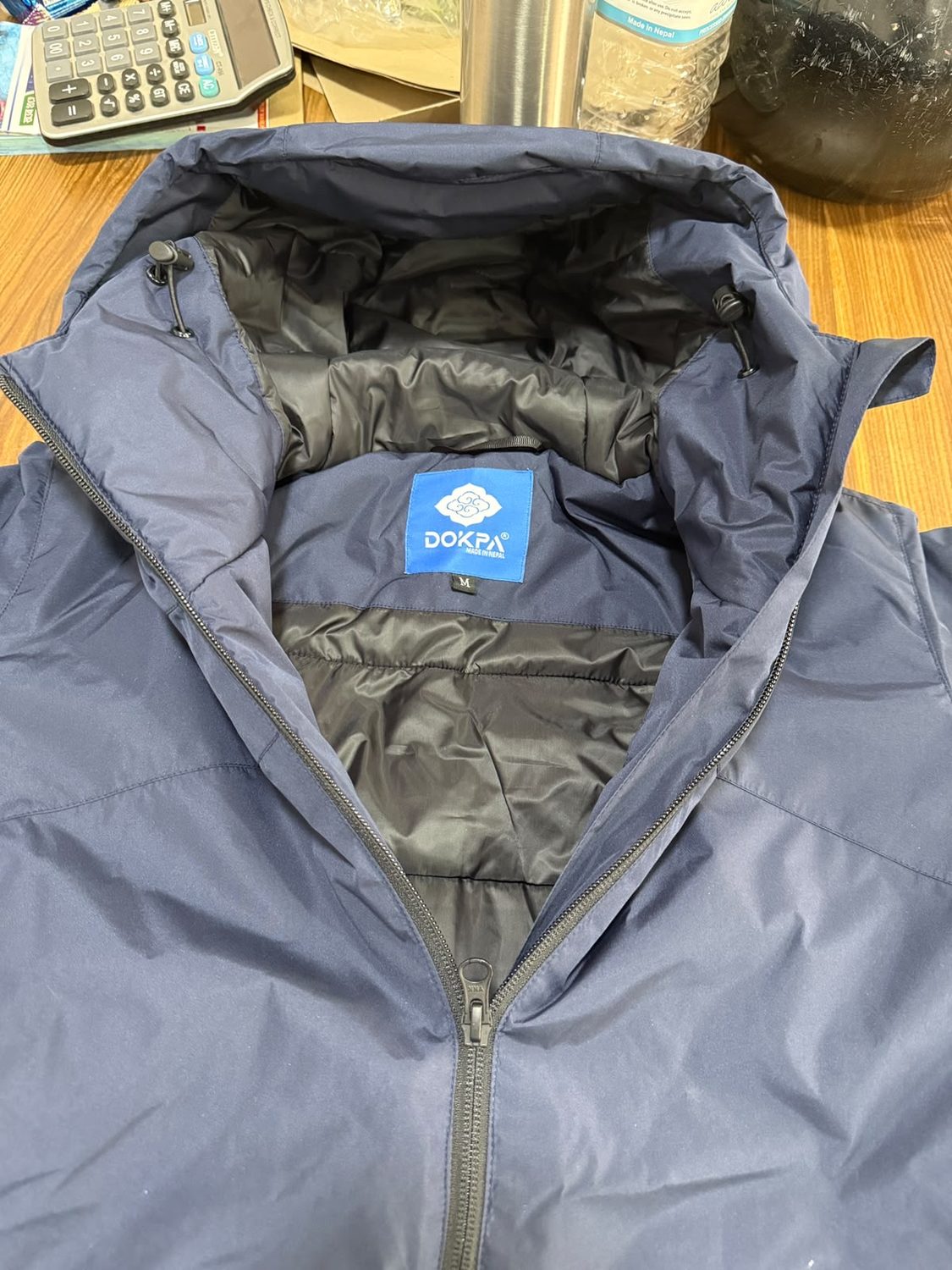 The blue Dokpa Made in Nepal woven label at an inside collar, below an open hood