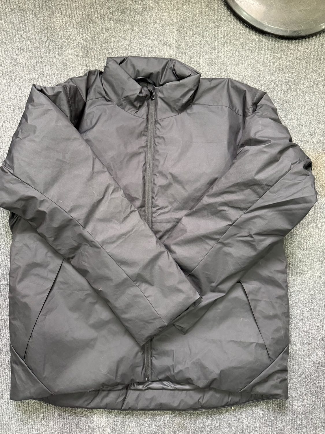 A grey shell jacket laid flat with a stand collar, front zip closed